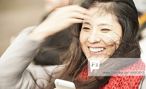 schöne Frau schaut auf ihr Handy bei windigem Wetter