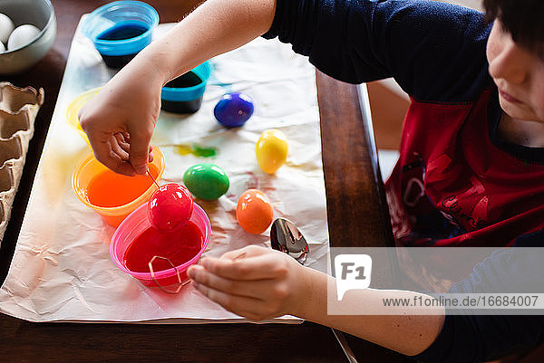 Nahaufnahme eines Jungen  der ein Ei in Farbe taucht  um es für Ostern zu färben.
