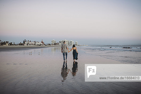 Mid-40's couple holding hands and walking barefoot along the beach