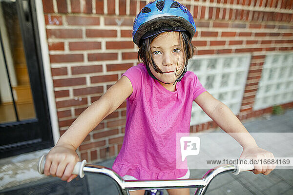 A cute little girl sits on her bike in front of house wearing a helmet