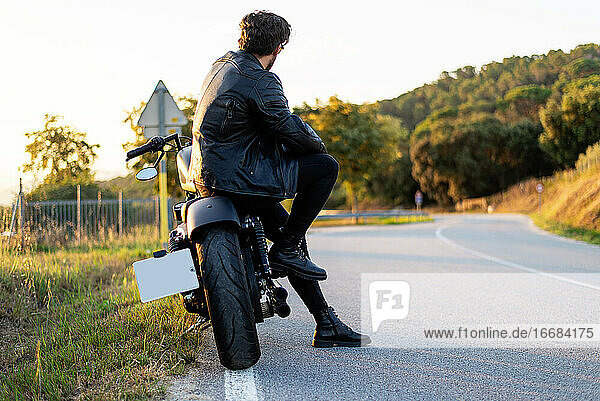 Rückansicht eines bärtigen Mannes  der auf einem Motorrad sitzt und auf die Straße schaut