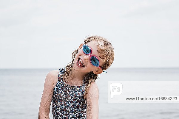 junges Mädchen lachend mit Schwimmbrille beim Spielen am Strand