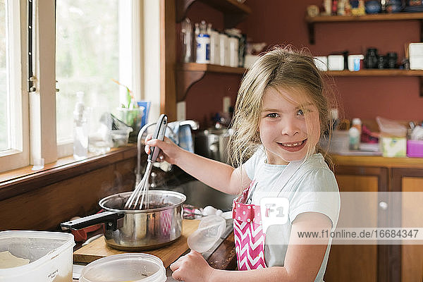 Young girl smiling and mixing hot baking mixture in messy kitchen