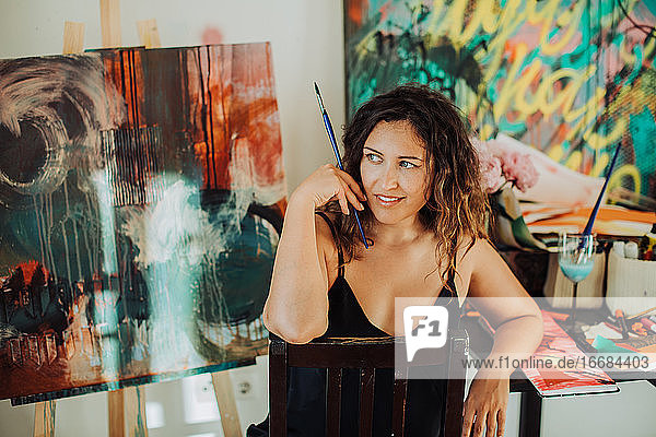 Junge Künstlerin sitzt im Atelier mit Leinwand im Hintergrund