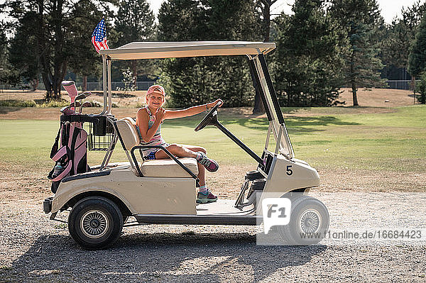 Junges Mädchen sitzt im Golfwagen mit rosa Golftasche an einem sonnigen Tag