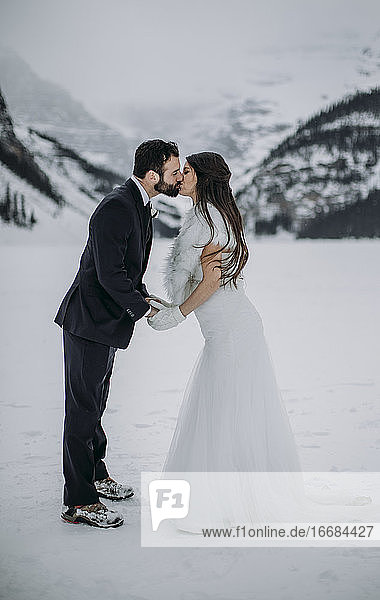 frisch verheiratetes Paar küsst sich auf dem zugefrorenen Lake Louise in Kanada