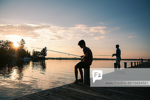 Vater und Sohn angeln auf einem Steg eines Sees bei Sonnenuntergang in Ontario  Kanada.