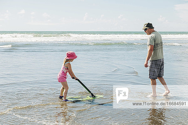 Young girl and her father playing on the beach with a skim board