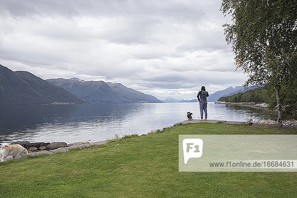 Ein Mann entspannt sich mit seinem kleinen Hund draußen an einem Fjord in Norwegen