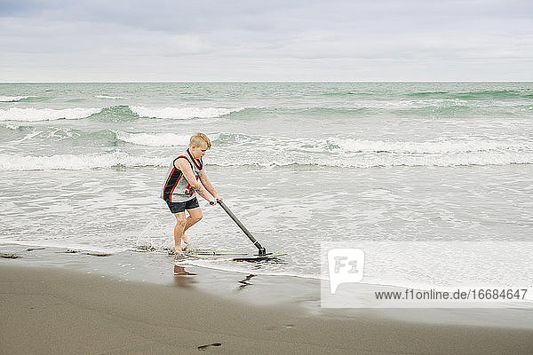 Young boy playing on the beach with his skim board