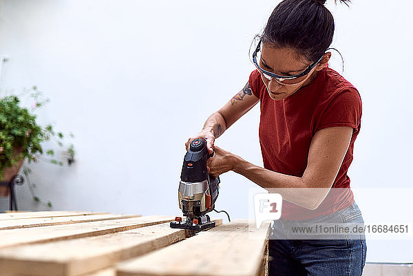 Eine junge Frau schneidet Holzpaletten mit einer Stichsäge
