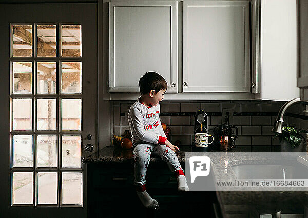 Kleiner Junge sitzt auf dem Tresen und freut sich  beim morgendlichen Kaffeekochen zu helfen