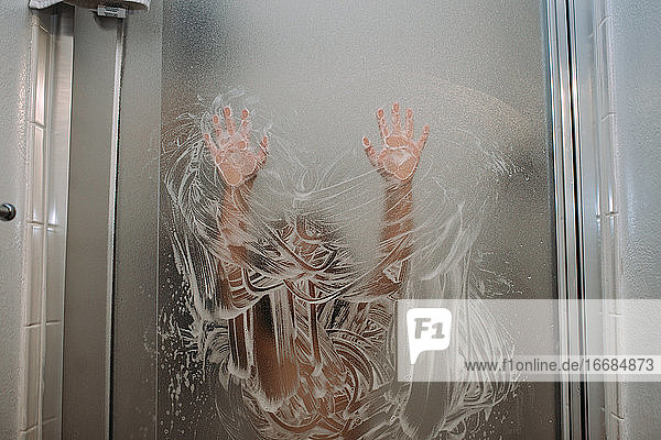 Kind spielt mit Seife an der Duschtür mit den Händen