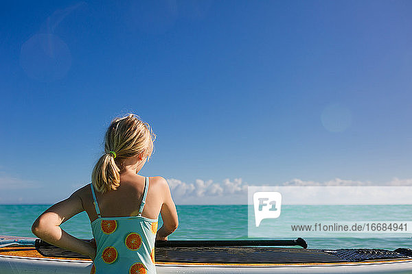 Junges Mädchen mit Paddleboard schaut auf ruhigen türkisfarbenen Ozean