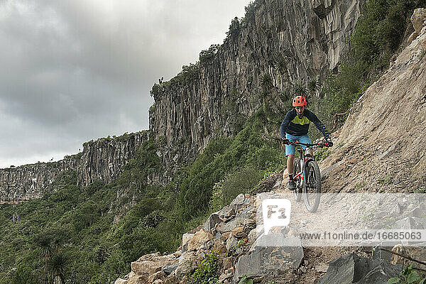 A man riding down a mountain bike on a narrow rocky trail at a canyon