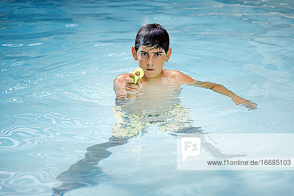 Hübscher  dunkelhaariger Junge  der mit einer Wasserpistole im Wasser des Pools spielt