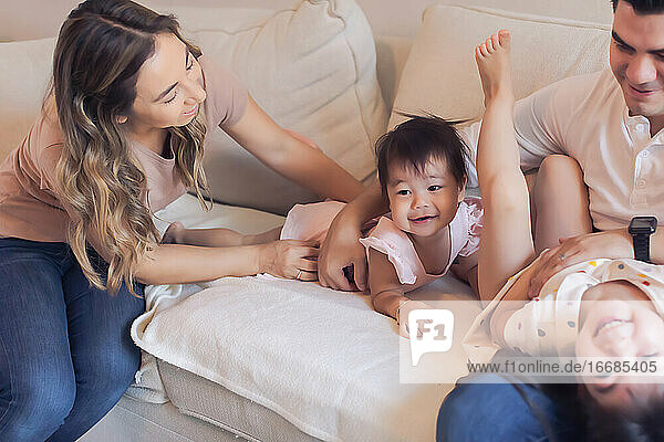 Family of four playing tickle fight on the couch at home.