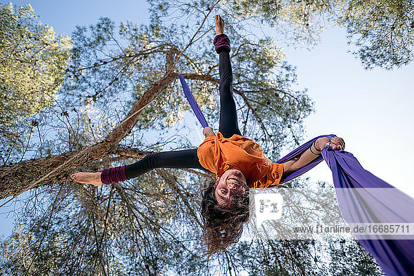 Junges Mädchen  Akrobatin. Übt Seiltanz in der Luft. Frau macht Zirkuskunststücke mit Kleidung im Wald. Straddle Fall Position.