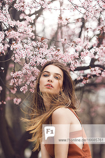 Fashion portrait of a young woman in front of the cherry blossom tree