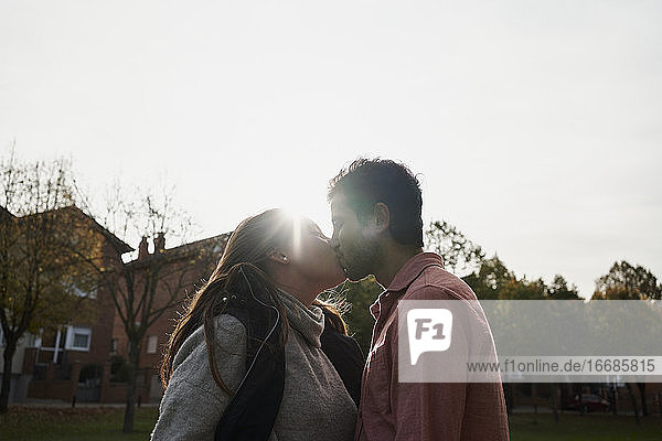 Schönes junges Paar  das sich bei Sonnenuntergang in einem Park küsst. Romantisches Konzept