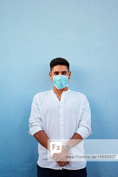 Junger lateinamerikanischer Mann mit Maske auf blauem Hintergrund