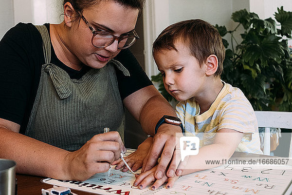 Mom painting her young son's finger nails at dining table