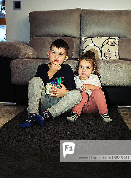 siblings watching a home movie while eating popcorn