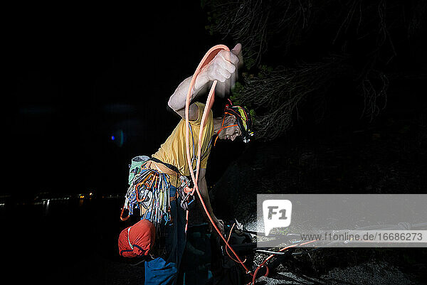 Mann beim Aufrollen des Seils nach einer nächtlichen Kletterpartie im Dunkeln mit einer Stirnlampe