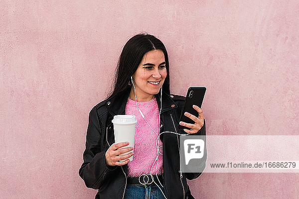 Young woman listen music and looks her smartphone in a pink background