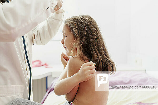Girl with a sad  tearful face while being examined by a doctor.