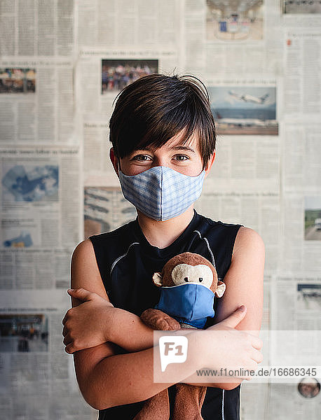 Young boy wearing mask holding toy monkey with newspaper backdrop.