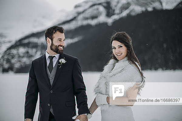 Bräutigam im Anzug blickt auf die frisch vermählte Frau im weißen Hochzeitskleid Winter