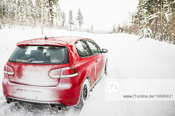 Rückansicht eines roten Sportwagens auf einer verschneiten Straße.
