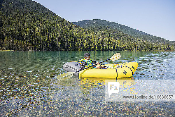 Young boy paddling yellow boat on scenic lake.