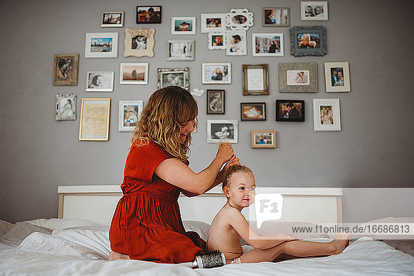 Mutter bürstet die Haare ihrer Tochter im Familienbett mit Fotos an der Wand