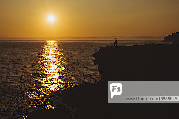 Junger Mann steht an der Klippe am Meer und beobachtet den Sonnenaufgang  Kantabrien  Spanien