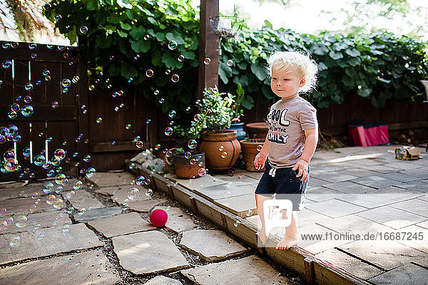 Two Year Old Boy Standing on Patio Playing with Bubbles