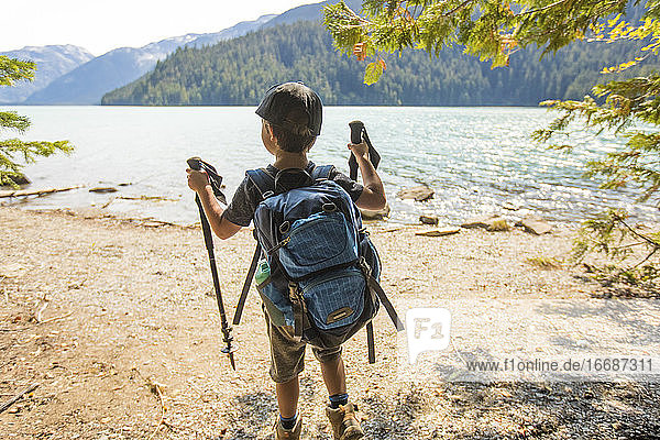 Rear view of young boy hiking by lake with backpack  hiking poles