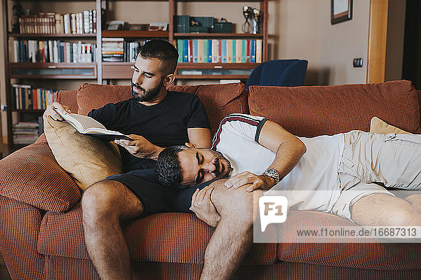 Junge liegt auf seinem Freund  während er auf dem Sofa ein Buch liest