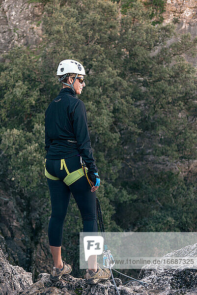 Concept: adventure. Female climber with helmet and harness. Thoughtful standing on a rock on top of the mountain. Solar luminous flare. Via ferrata in the mountains.