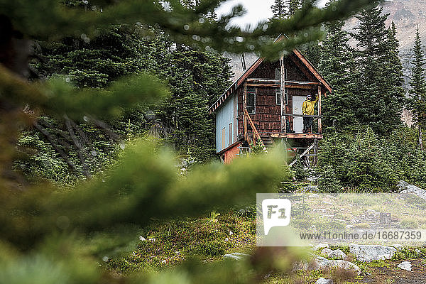 Hiker man standing on porch of old house in forest while hiking in BC