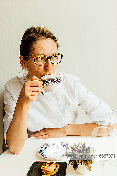 Frau in weißer Uniform trinkt Cappuccino am Tisch in einem Cafe