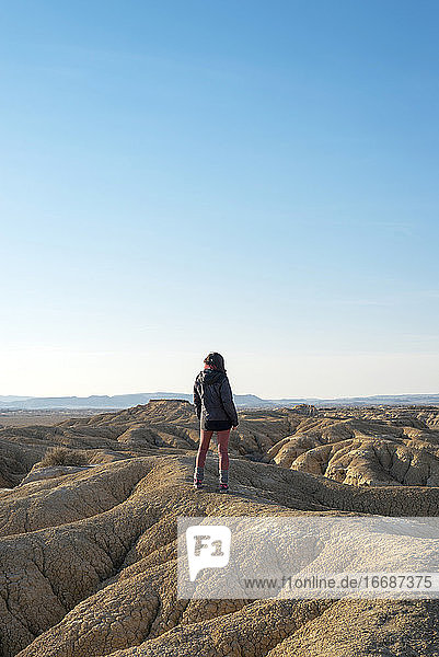 Rückansicht einer Frau  die auf einem Hügel in einer Wüstenlandschaft vor blauem Himmel steht