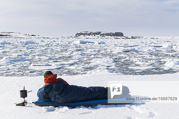 Männlicher Wanderer  der im Schlafsack auf schneebedecktem Land ruht
