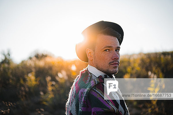 Mann im Poncho posiert gegen die Sonne in ländlicher Umgebung  schaut in die Kamera