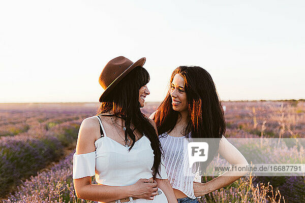 Freundinnen  die sich lächelnd in einem Lavendelfeld anschauen