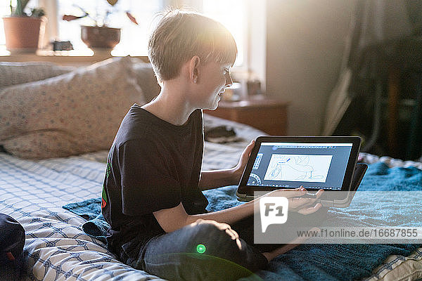 Junge Person zeigt auf dem Bett sitzend Kunst  die auf einem Tablet-Computer gemacht wurde