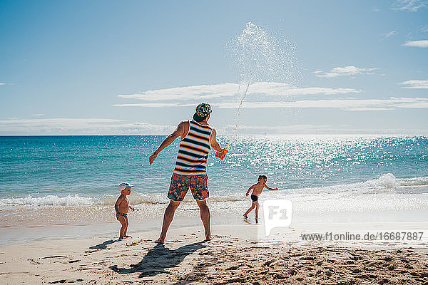 Kids playing with water at the beach with their dad on a sunny day