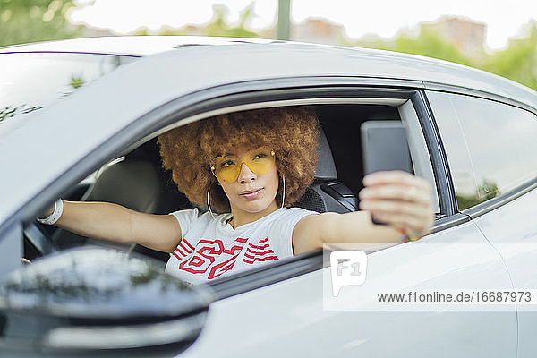 Frau mit Afro-Haar  die ein Foto mit ihrem Smartphone neben ihrem Auto macht