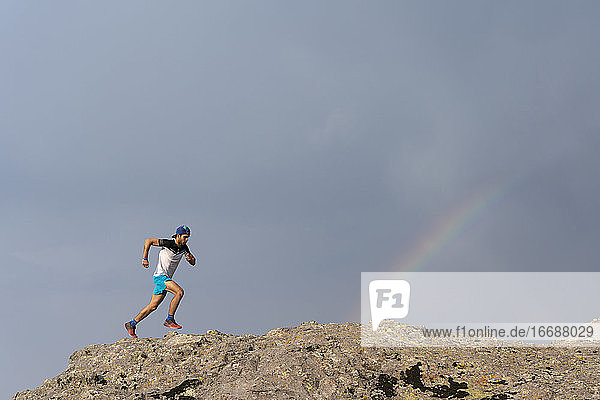 One man trail running on a rocky terrain with a rainbow